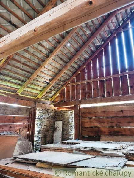 Interior of a wooden structure from Pozemkov - living with a sloped roof and rock wall.