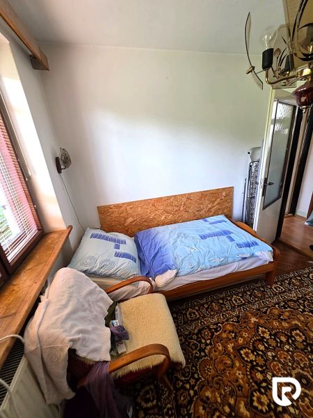 A room in a family house with an old carpet, an armchair, and a bed by the window.