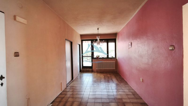 A hallway with ceramic tiles, pink walls, a window, and a chandelier in a family house.
