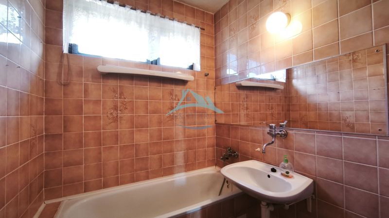 A family house bathroom with a bathtub, a sink, and tiled walls in a brown shade.