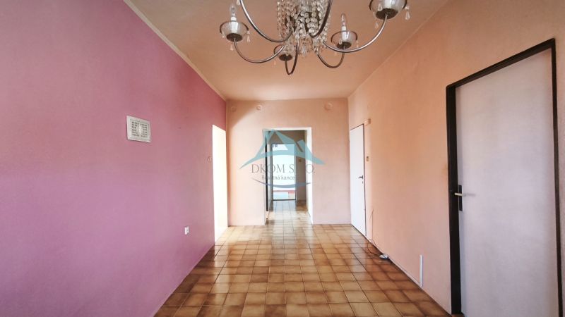Interior of a family house with a chandelier, pink wall, and tiled floor.
