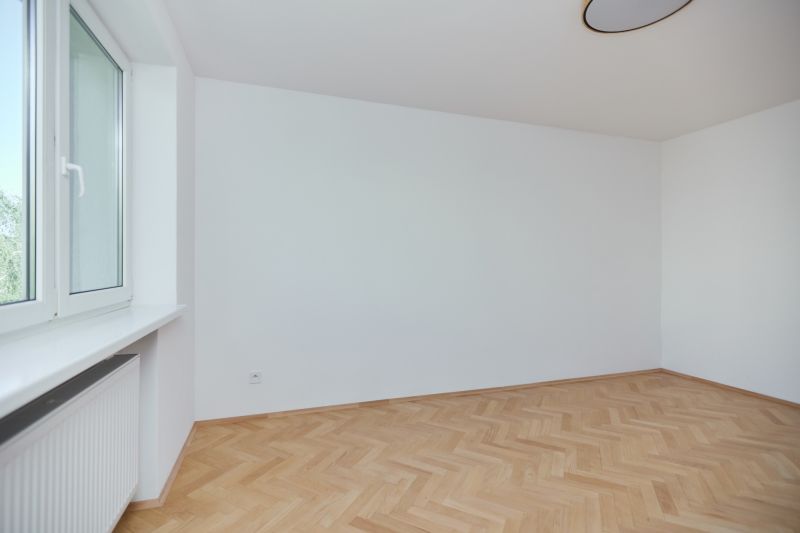 An empty room with a wood-patterned floor in a three-room apartment.