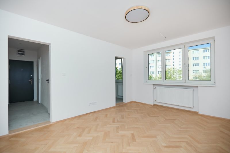An apartment with a wooden floor design, white walls, and large windows.