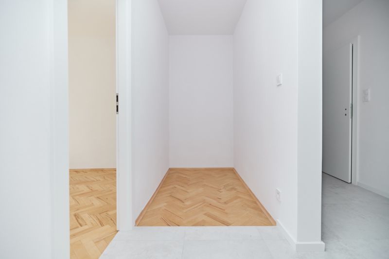 A narrow hallway with white walls in a 3-room apartment and a floor with a wooden decor.