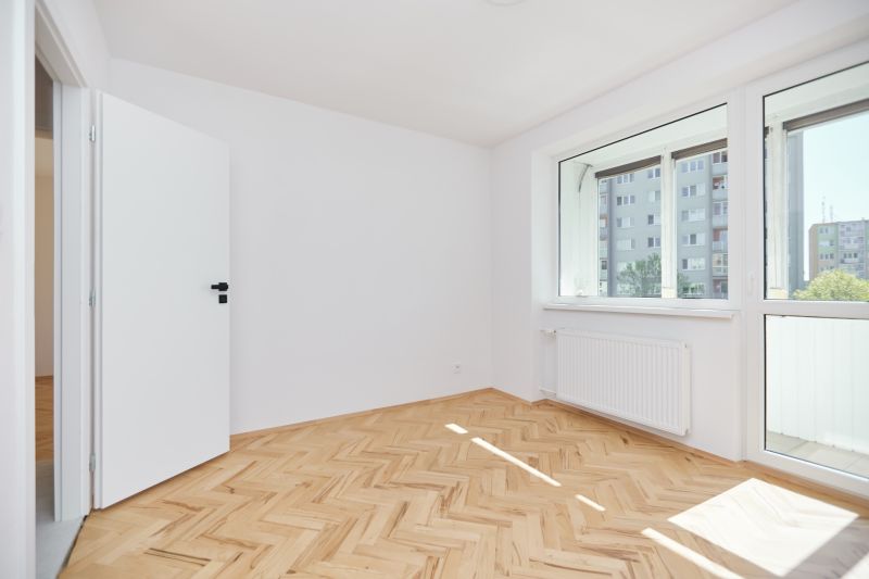 A room in a three-room apartment with a wooden decor floor and a large window.