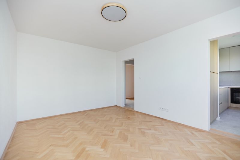 An empty room with wooden floor decor and a view into the kitchen in a 3-room apartment.