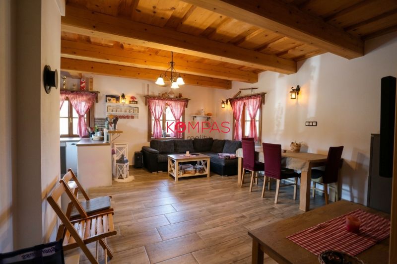 The living room of a family house with wooden ceilings, a floor with a wood pattern, and red curtains.