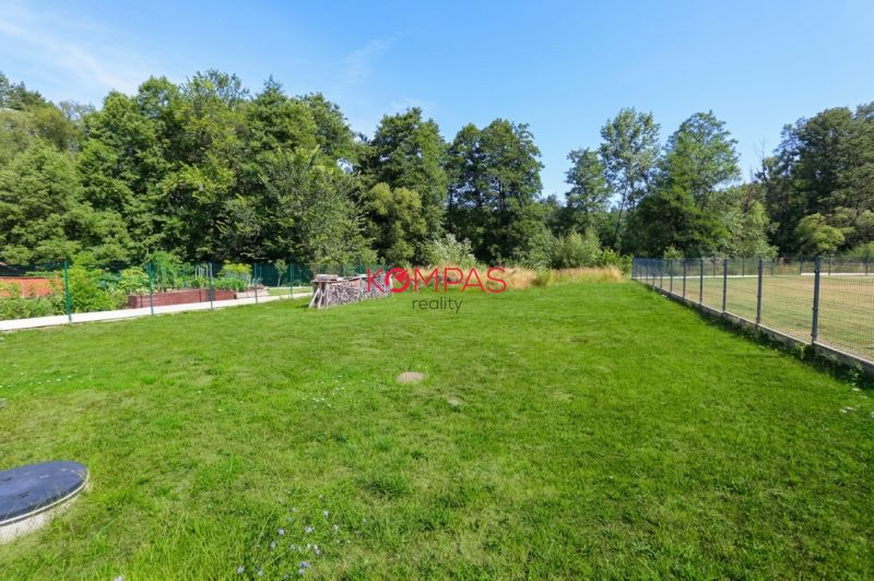 The garden of a family house in Očová with a lawn and fencing, surrounded by forest.
