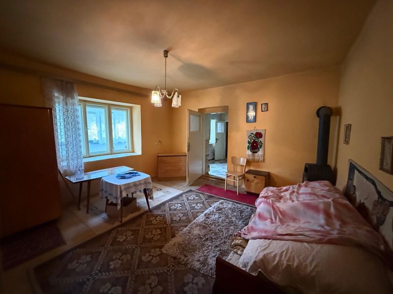 The interior of a family house with a bed, table, and wood stove, styled in warm tones.