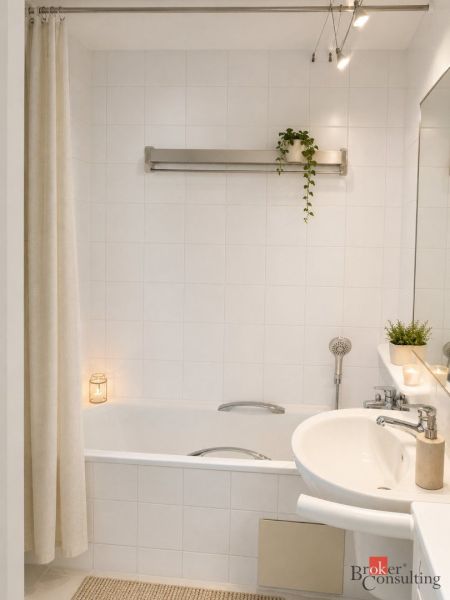 A bathroom with a bathtub, a sink, a plant, and white tiles in a 2-room apartment.