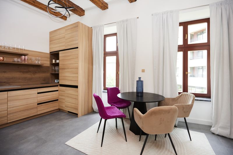 A kitchen corner in a 3-room apartment with colorful chairs and a wooden-patterned floor.