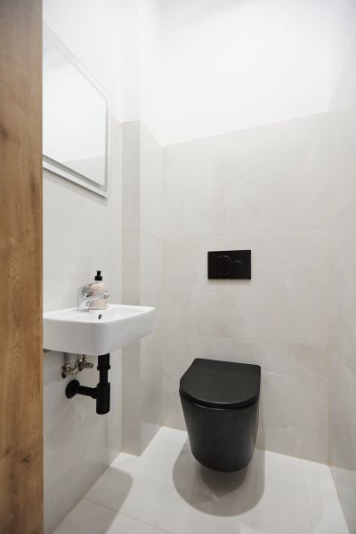 A bathroom with a black toilet, sink, and mirror in a three-room apartment.