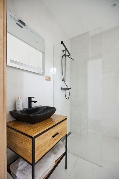 A bathroom in a 3-room apartment with a black sink, shower, and wooden decor.