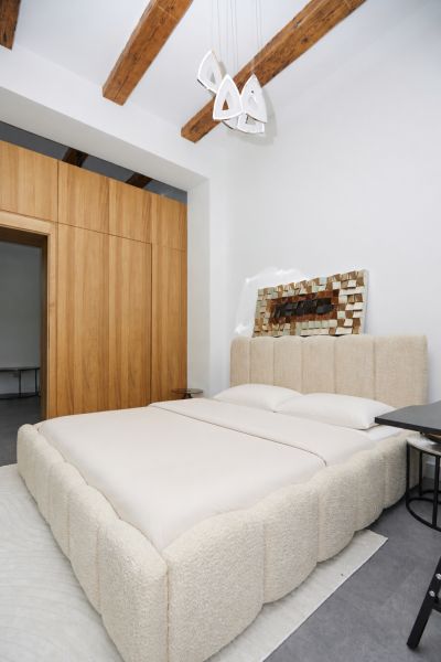 A bedroom in a 3-room apartment with wooden ceiling beams and a spacious bed.