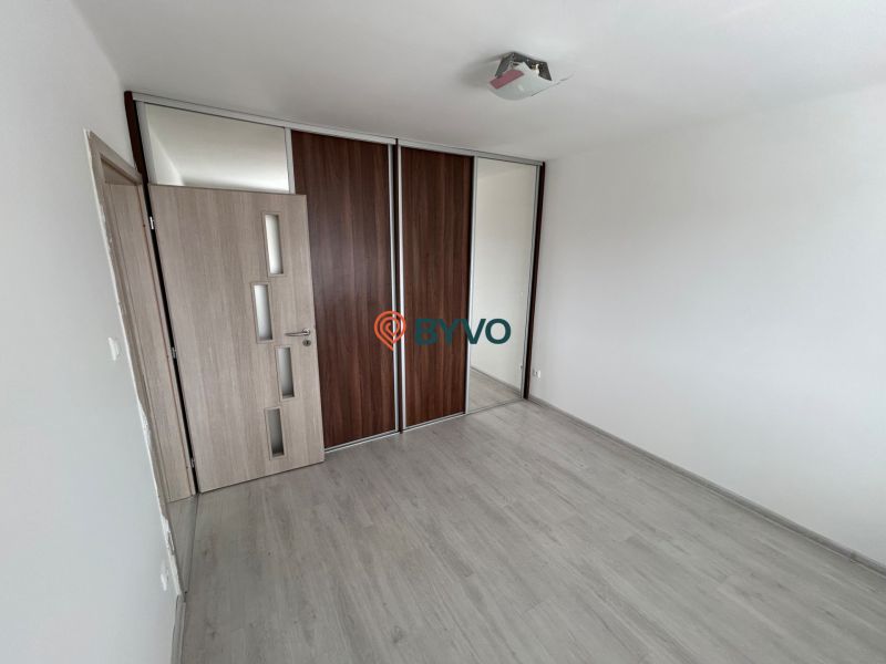 An empty room in a 3-room apartment with a wooden decor floor and a built-in wardrobe.