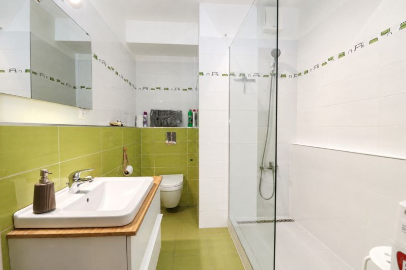 A bathroom in a 2-room apartment with a sink, green tiles, and a shower corner.