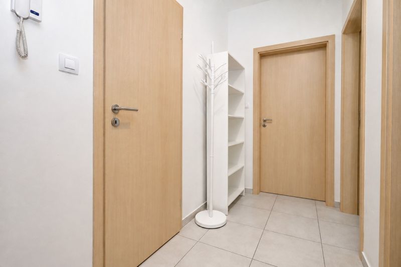 In the hallway of the 2-room apartment, there is a white shelf and a coat rack on light-colored tiles.