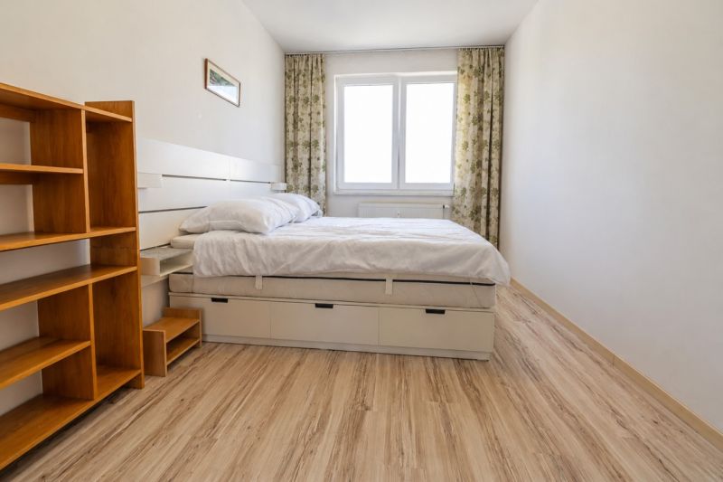 A bedroom in a two-room apartment with a bed, a shelving unit, and a floor with a wood decor.