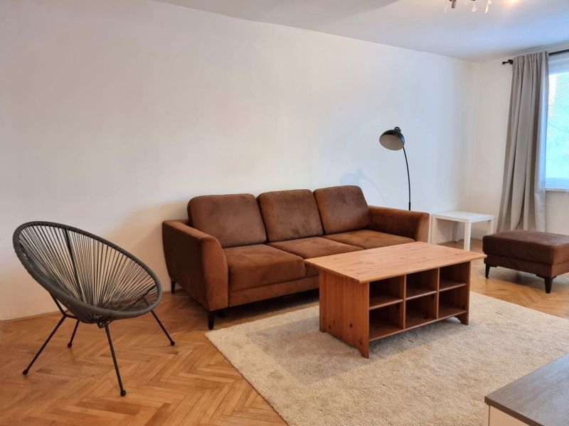 Living room of a two-room apartment with a brown sofa and a floor with a wooden decor.