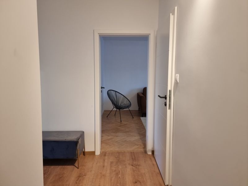 A hallway in a 2-room apartment with a wooden decor floor and a view into the living room.