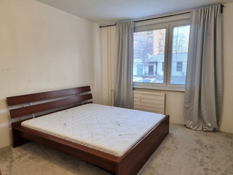A bedroom with gray curtains, a large window, and a bed in a two-room apartment.