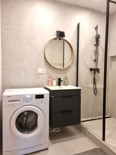 A bathroom with a washing machine, shower cabin, and round mirror in a 2-room apartment.