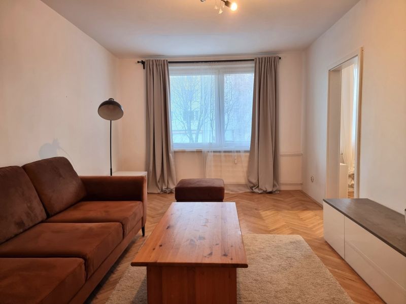 Living room in a two-room apartment with a sofa, table, and wooden decor flooring.