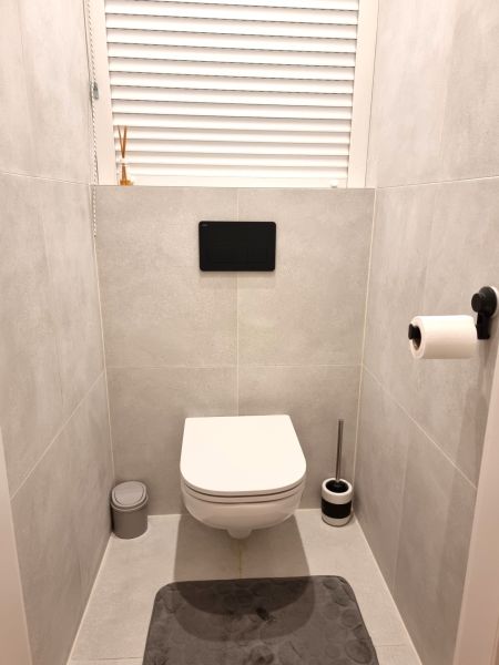 Bathroom in a 2-room apartment with a modern wall-hung toilet on light tiles.