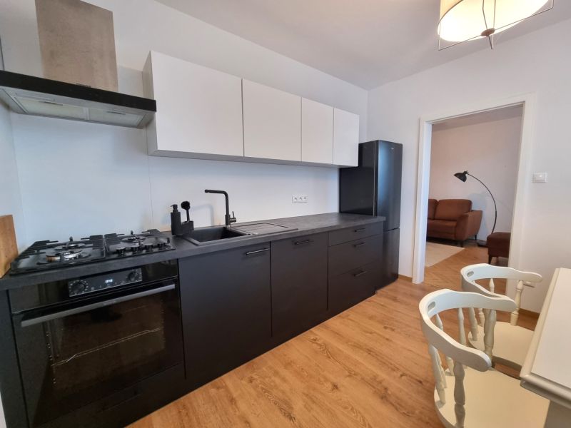 A kitchen in a 2-room apartment with black appliances and a wooden decor floor.