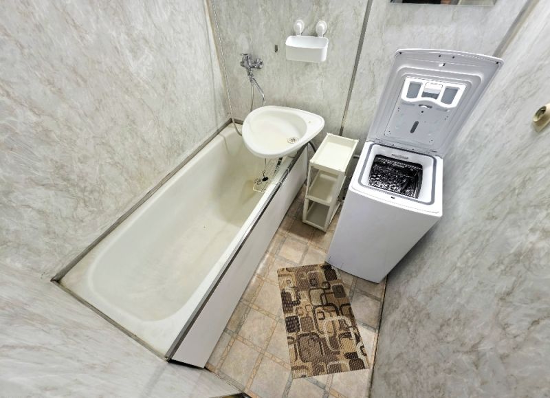 A bathroom in a 3-room apartment with a bathtub, washing machine, and tiles.