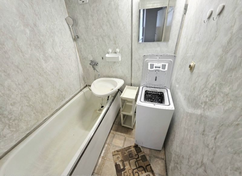 A bathroom with a bathtub, toilet, washing machine, and mirror in a 3-room apartment.