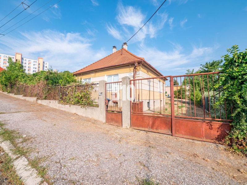 A family house in Nitra with a fence and a sloped roof, with a block of flats in the background.