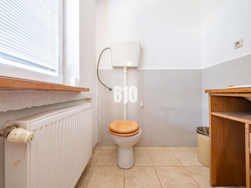 A toilet with a window, radiator, and storage space in a family house.