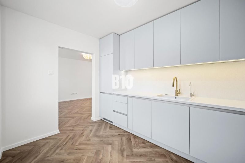 A kitchen in a 3-room apartment with white furniture and a wooden decor floor.