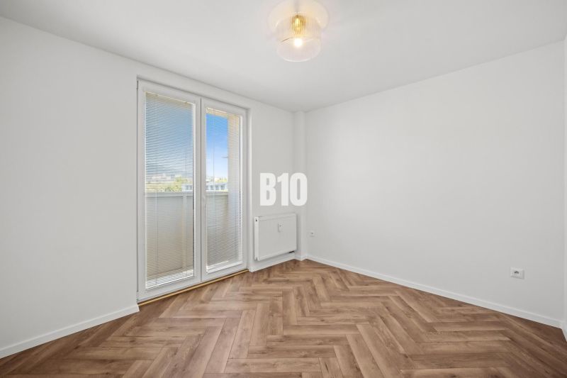 An empty room with a wooden decor floor and balcony doors in a 3-room apartment.