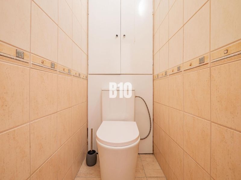 A toilet with beige tiles in a studio apartment, practical design and storage space.