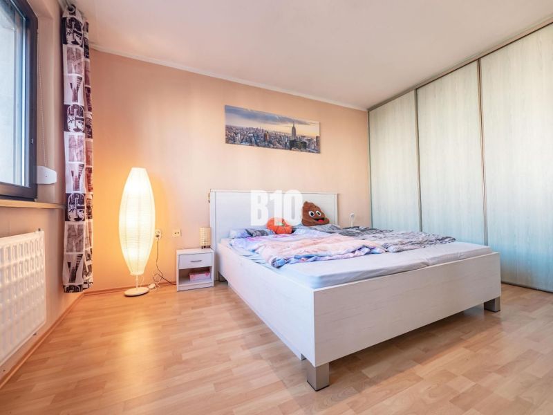 A bedroom with wood-patterned flooring, a bed, and a wardrobe in a studio apartment.