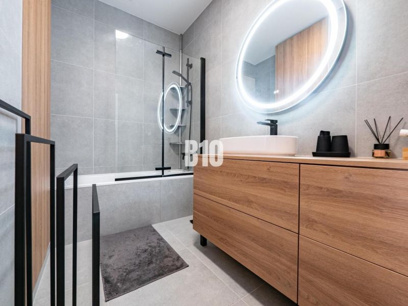 A bathroom with wooden decor in a family house, featuring a bathtub and an oval mirror with lighting.