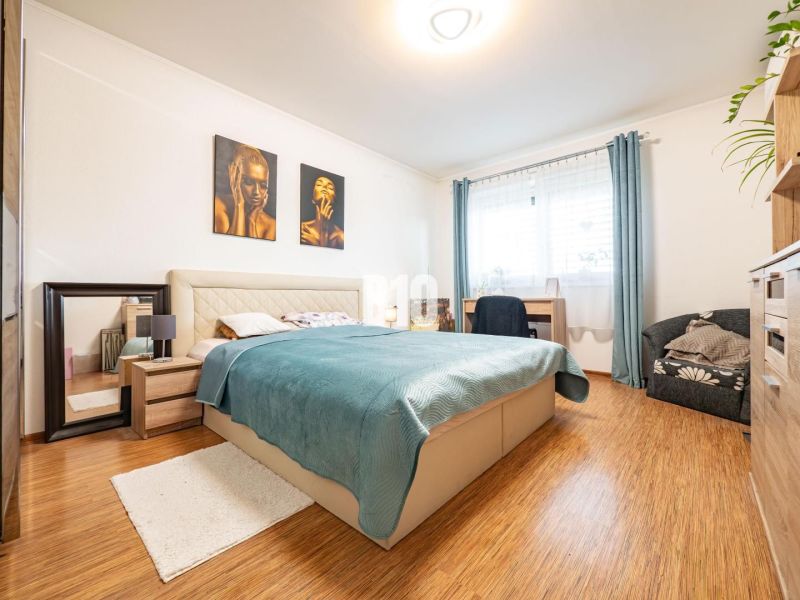 Bedroom in a family house with a bed, mirror, and wooden decor flooring.