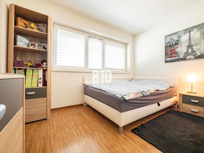 A bedroom in a family house with a wooden decor floor and a shelf full of books and toys.