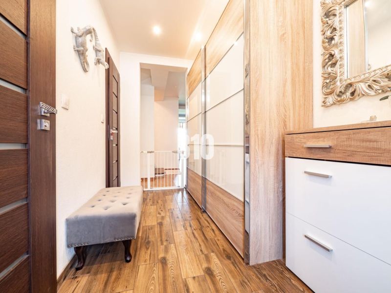 A hallway with a wooden decor floor, cabinets, and a mirror in a family house.