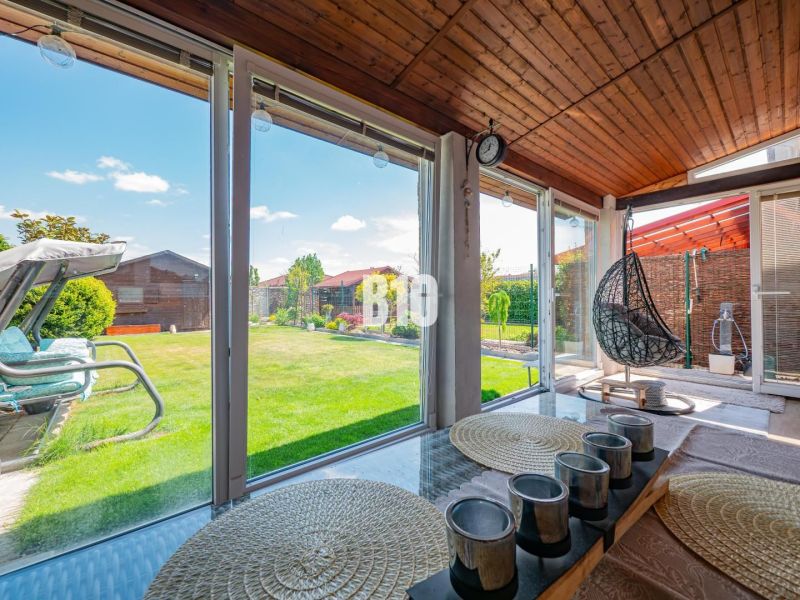 A glazed terrace of a family house in Nitra with a view of the garden and wooden decor.