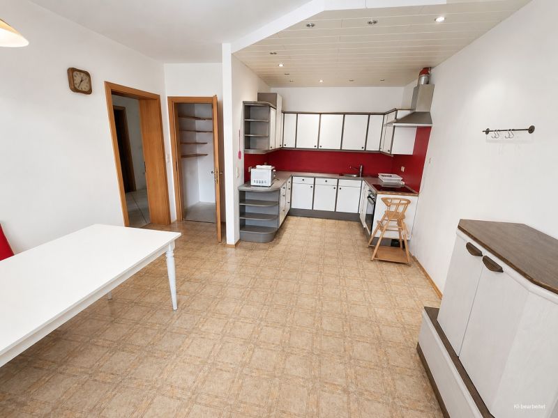 A kitchen in a family house with red accents and a wood-patterned floor.