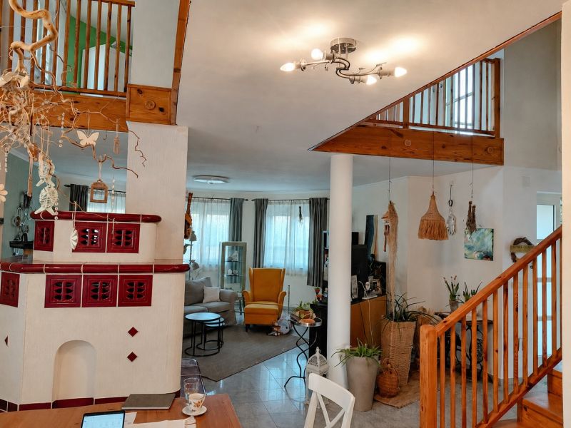 Interior of a family house with a ceramic fireplace, plants, and wooden stairs.