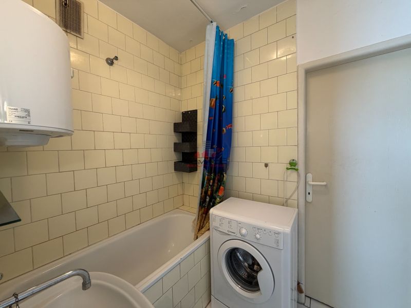 A bathroom in a 3-room apartment with a bathtub, a washing machine, and white tiles.