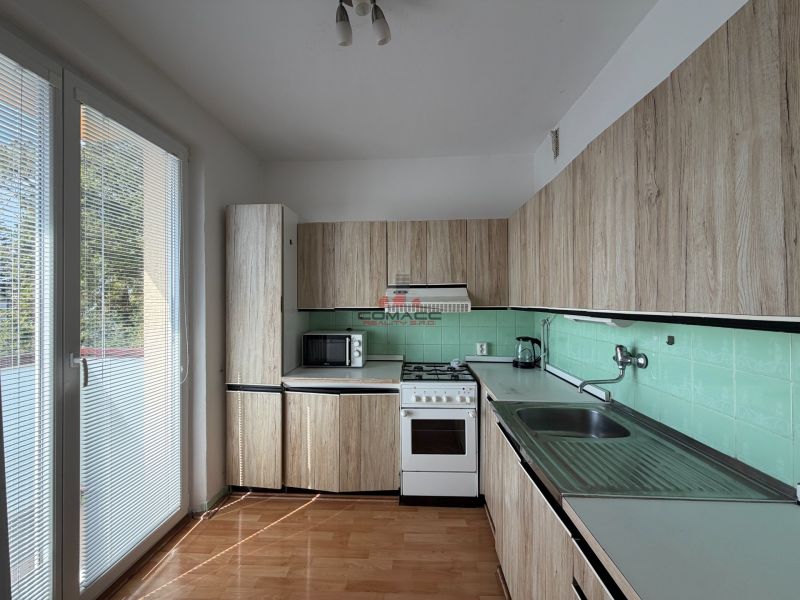 A kitchen in a 3-room apartment with a wood-patterned floor and direct access to the balcony.
