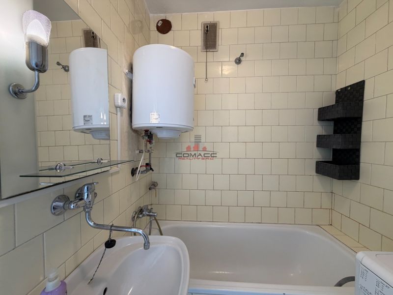 A bathroom in a 3-room apartment with a bathtub, a sink, and a water heater.
