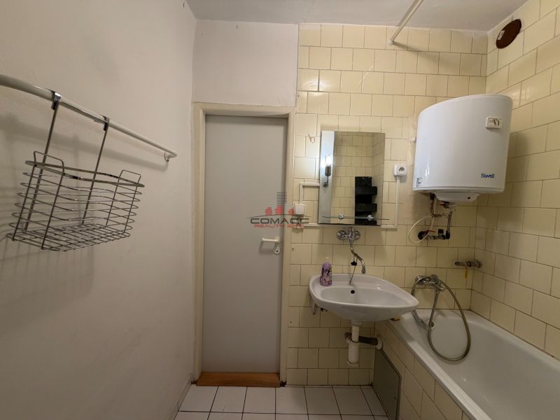 A bathroom in a 3-room apartment with a sink, a bathtub, and a water heater on the wall.