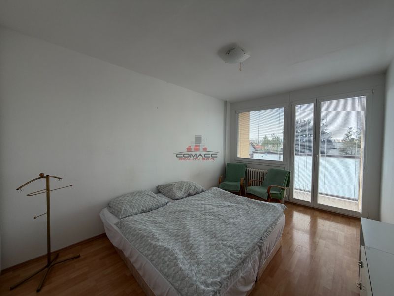 A bedroom in a 3-room apartment with a wooden decor floor, a bed, and chairs.