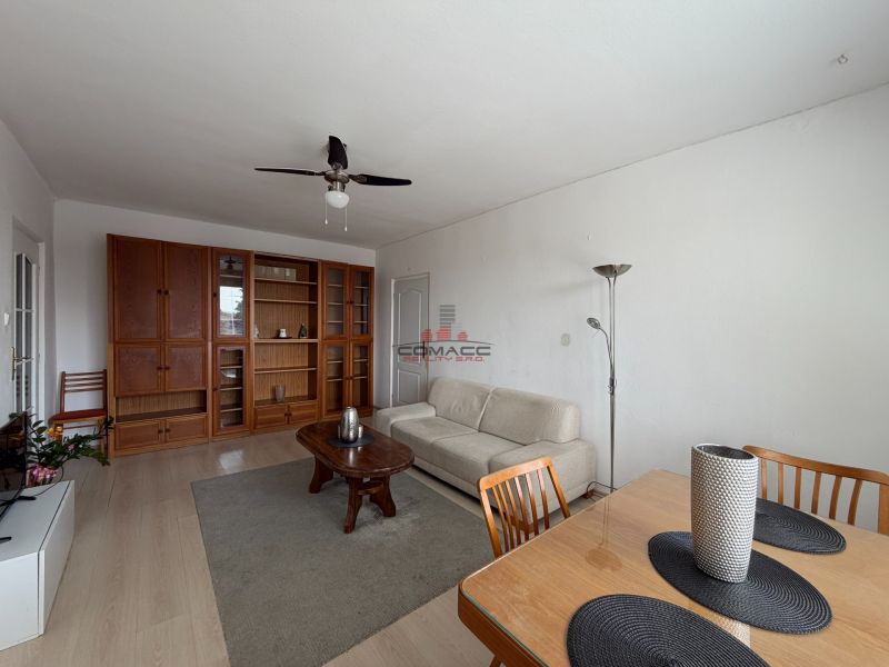 Living room with wood-patterned flooring, a sofa, and a dining table in a three-room apartment.